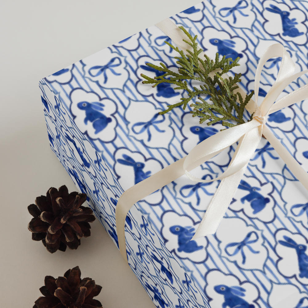 Gift box wrapped in blue and white patterned paper with a bow, surrounded by pine cones on a light background.
